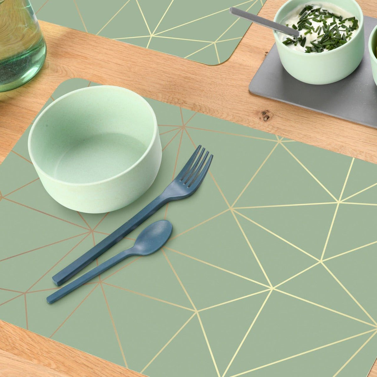 Tischset Geometrie in Salbeigrün mit feinen goldfarbenen Linien, dazu Schale und Besteck unerquicklich